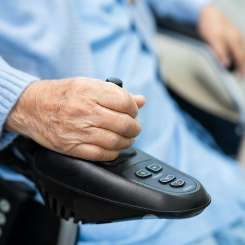 Asian senior woman patient on electric wheelchair with remote control at hospital.